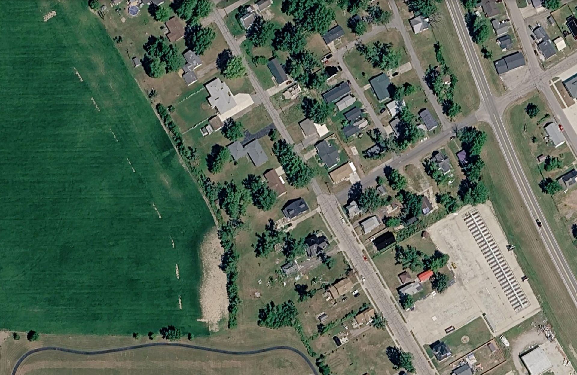 Aerial view of a suburban neighborhood beside a large green field and a road