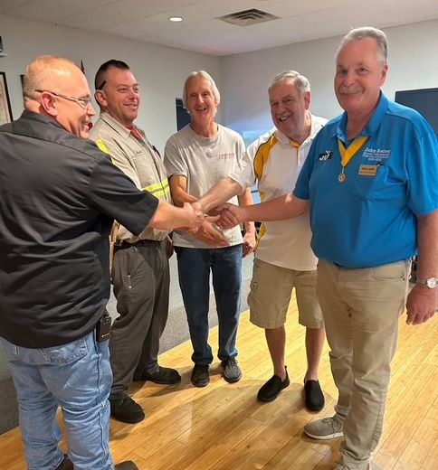 Five men in casual clothes shake hands in a bright office room.