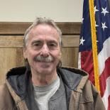Smiling man standing indoors beside an American flag and wood-paneled wall
