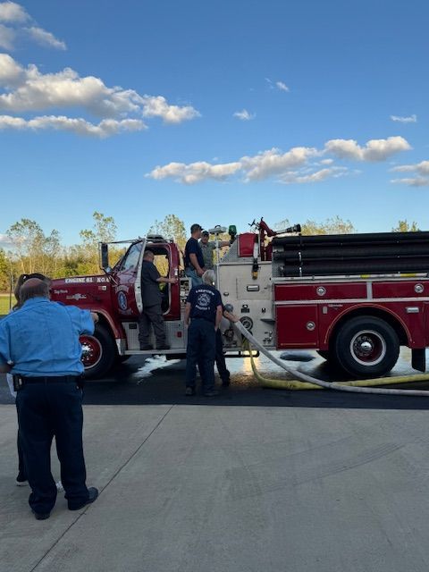 Fire truck with several people gathered around it on a sunny roadside.