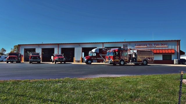 Fire station with several red fire trucks parked outside under a blue sky.