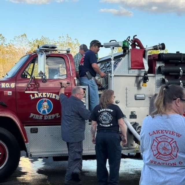 Firefighters gathered beside a red Lakeview fire truck under a clear blue sky