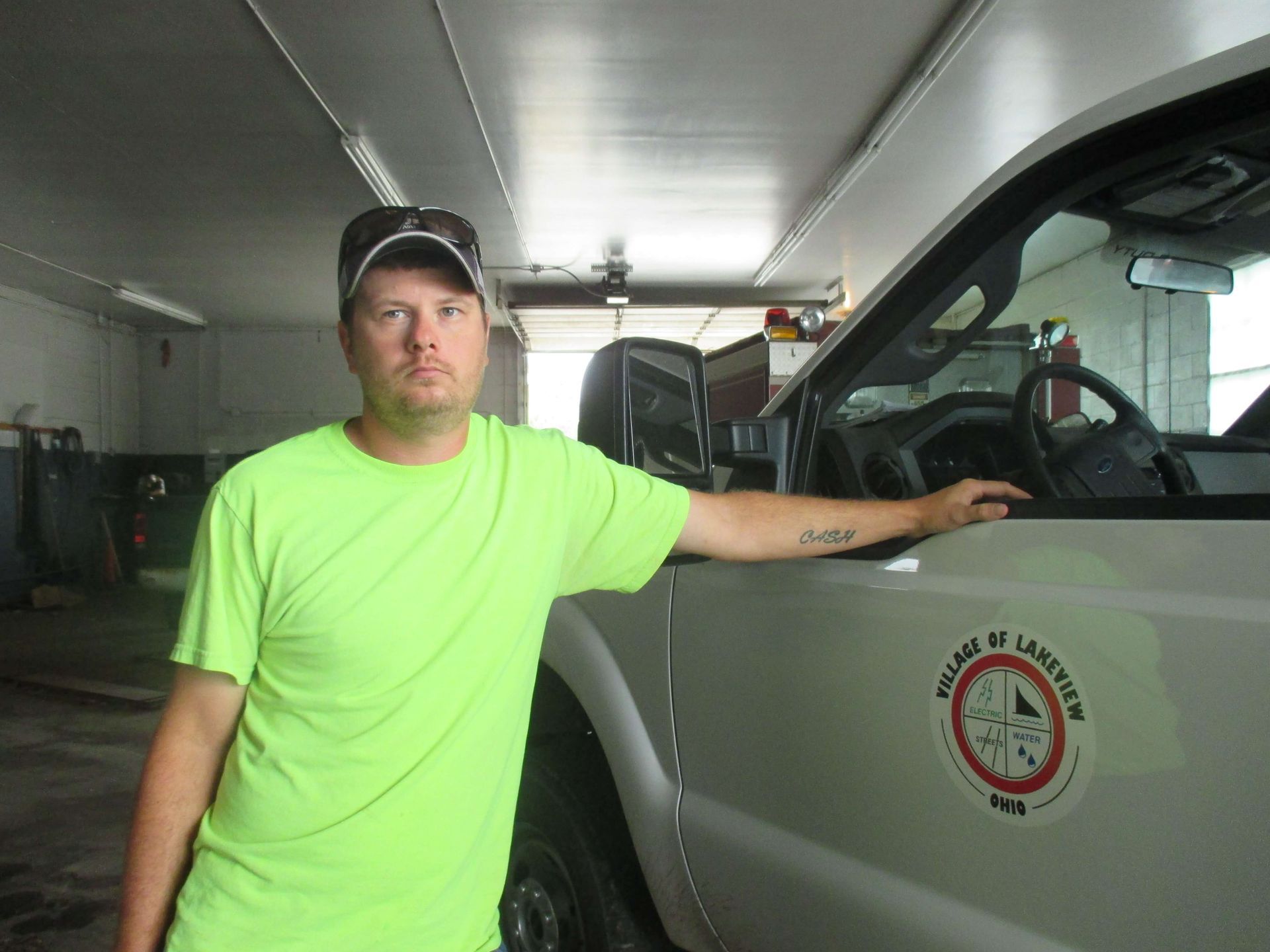 Man in neon green shirt leaning on a white truck inside a garage