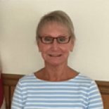 Smiling person in glasses and striped shirt against a plain indoor background