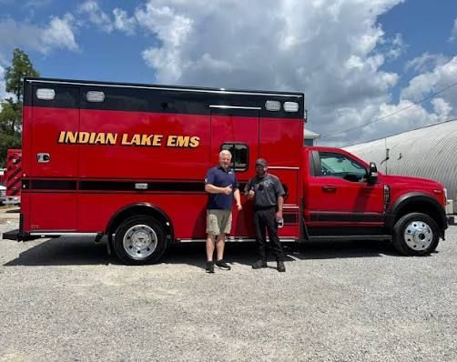 Two men standing beside a red Indian Lake EMS truck in a gravel lot