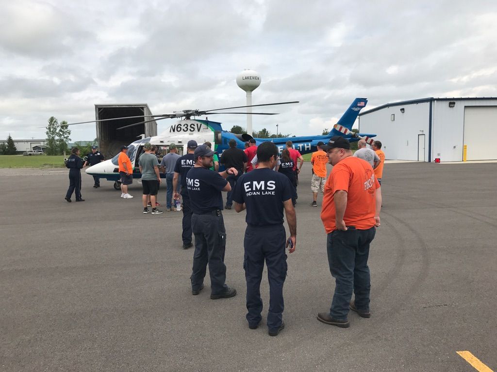 People gathered on an airport tarmac near a small plane and emergency responders in orange and navy uniforms.