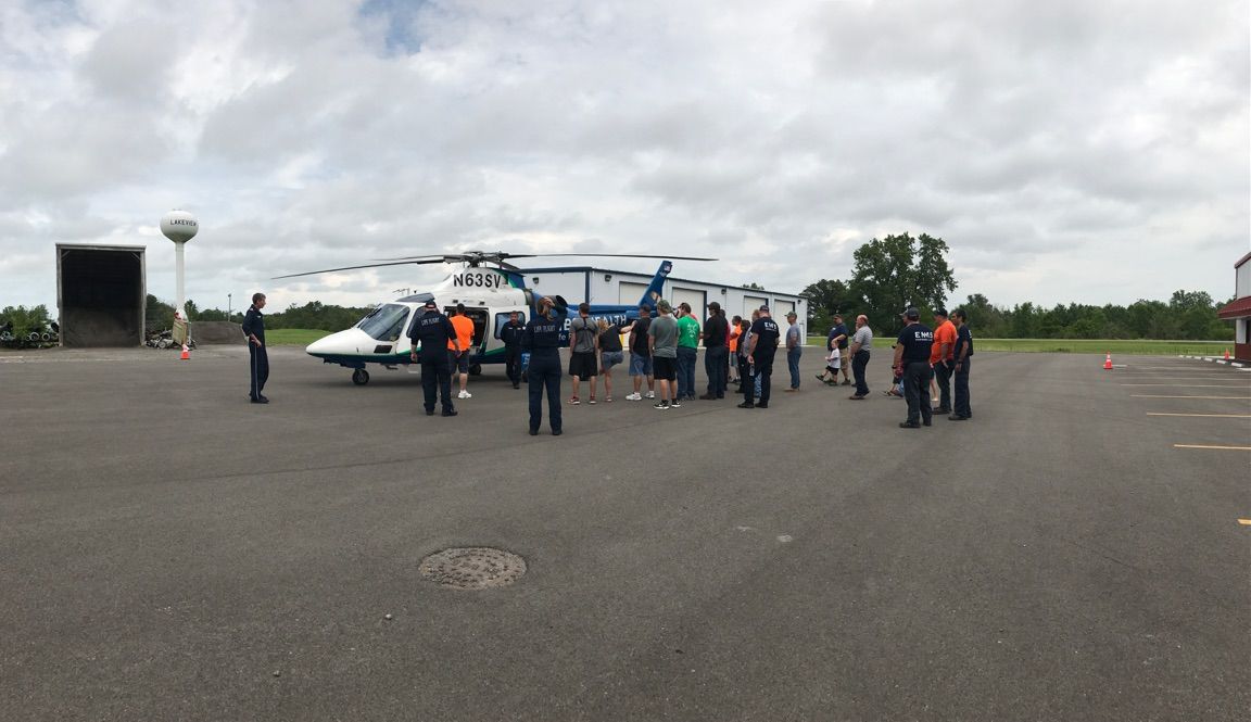 People gathered around a small white airplane on a runway under a cloudy sky