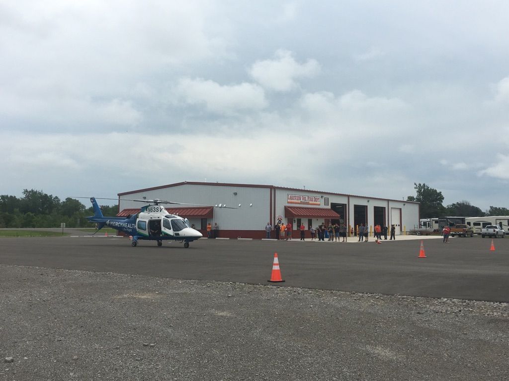 Helicopter on a gravel airfield beside a small hangar under cloudy skies
