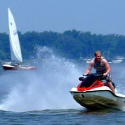 Jet ski rider splashing through water near a sailboat on a lake