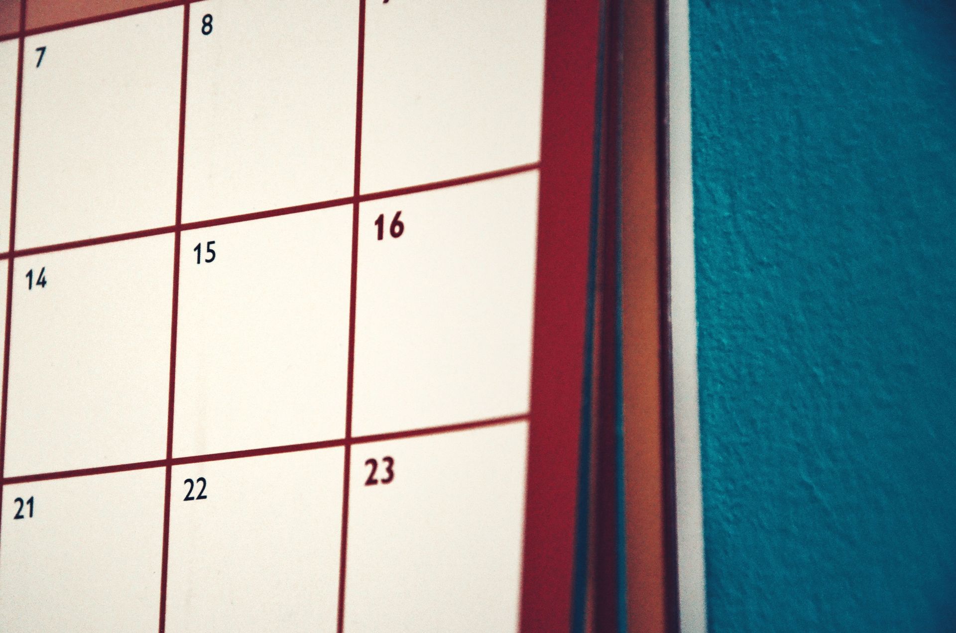 Close-up of a white wall calendar with black numbers beside a teal wall and red frame