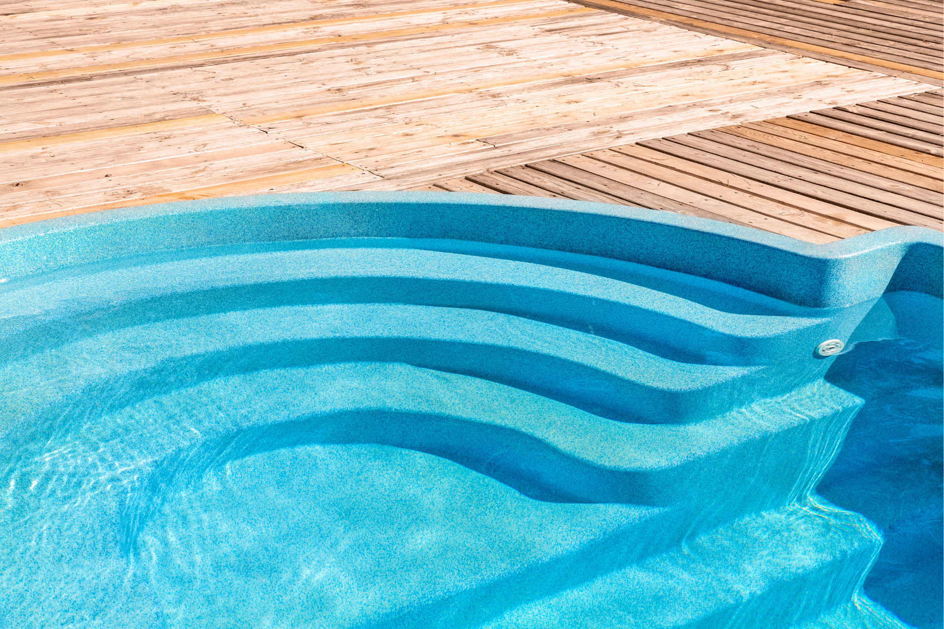 Blue pool steps with water, next to a wooden deck.