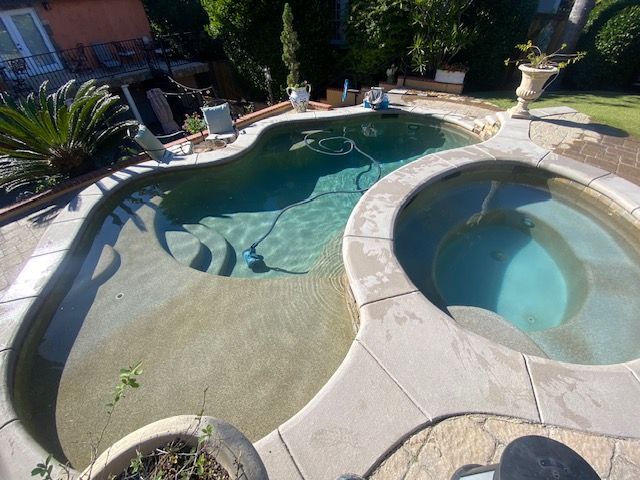 Swimming pool with connected hot tub, light-colored concrete surround, steps, and pool cleaner.