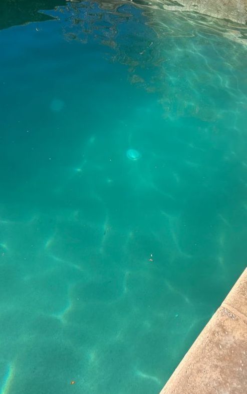 Turquoise pool water with rippling sunlight. A stone ledge is in the lower right corner.
