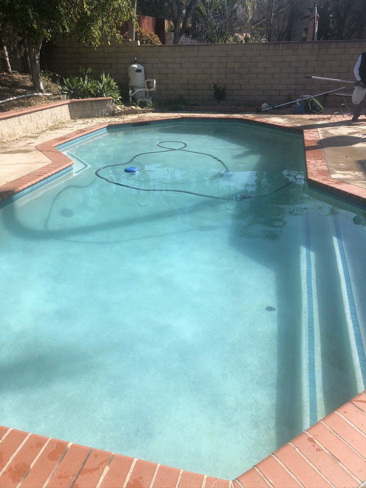 Pool with blue water and brick edging. A pool cleaner floats inside. Outdoor setting.