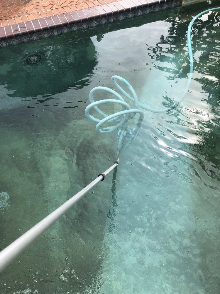 Cleaning a pool with a net and pole; turquoise water, brick edge.