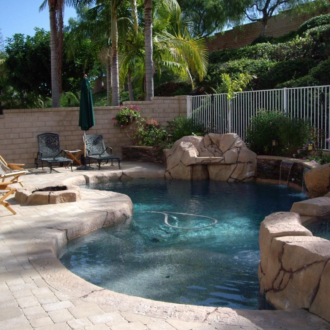 Swimming pool with rock waterfall feature and lounge chairs in a backyard setting.