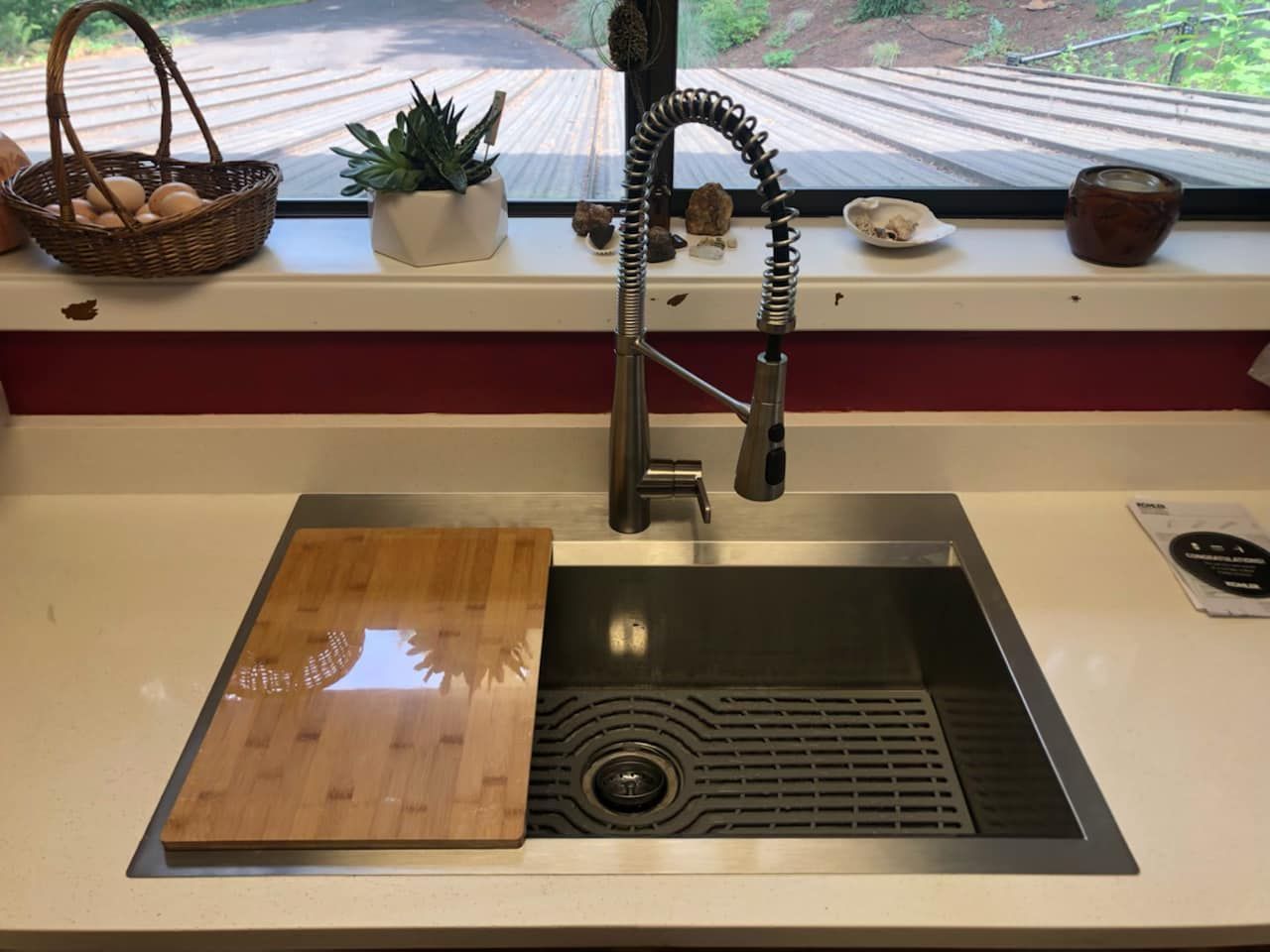 A kitchen sink with a wooden cutting board underneath it