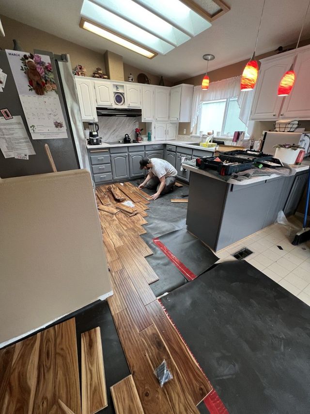 A man is laying wooden flooring in a kitchen in Eugene, Oregon after water leak damaged prior flooring layout