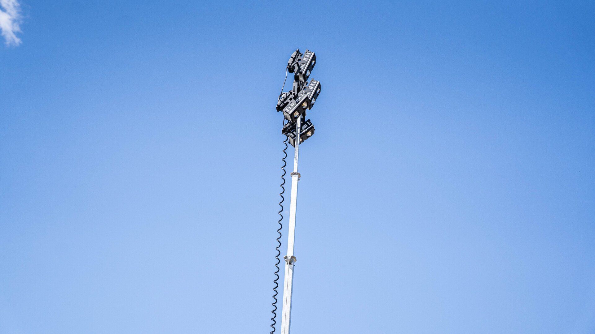 Orange mobile light tower with four lights on a telescopic mast, outdoors.