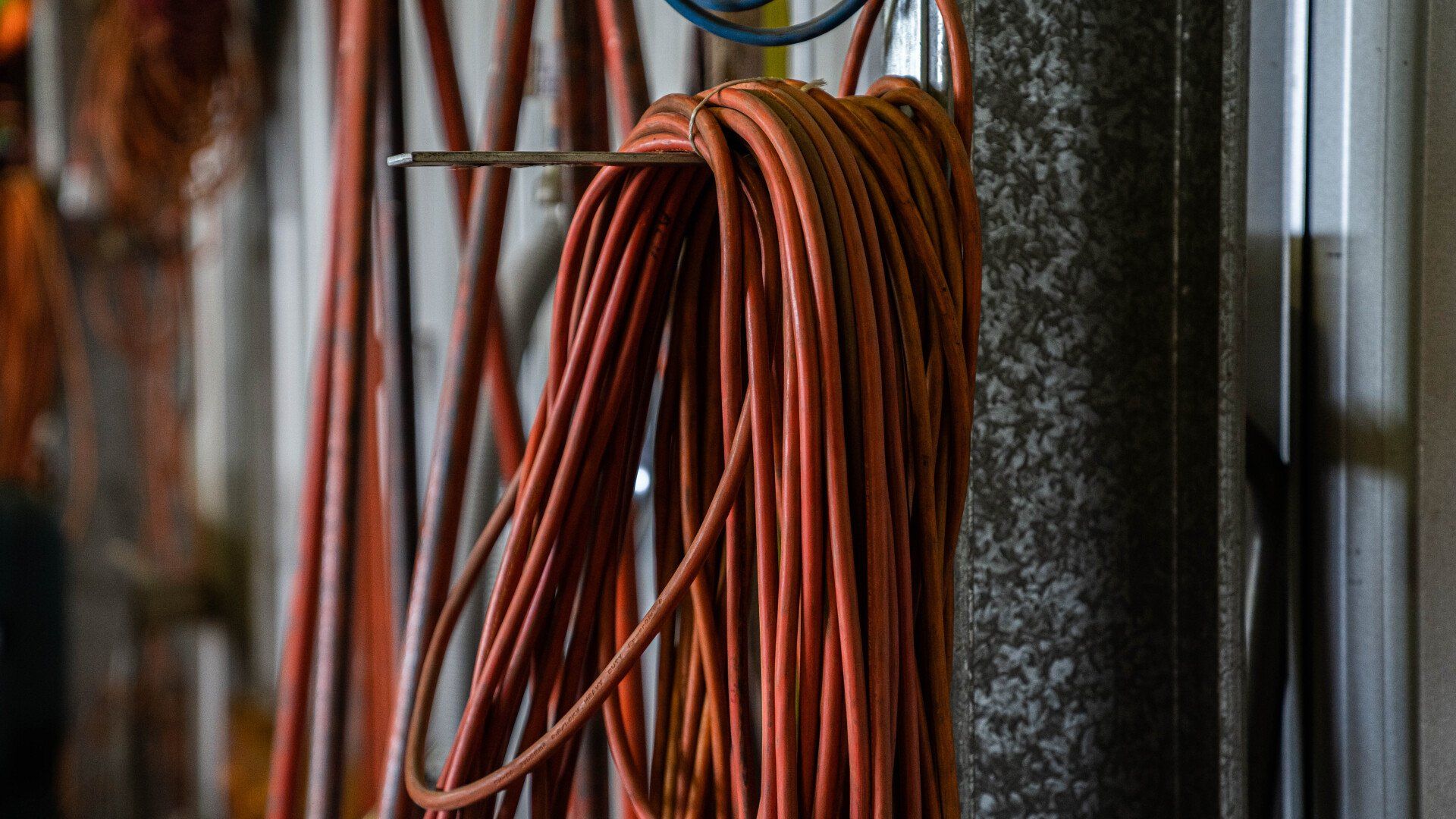Coiled orange electrical cord hanging on a hook in a workshop.