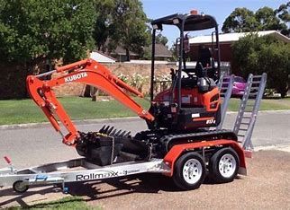 Orange Kubota mini excavator on a trailer, ready for transport. Outdoors, daytime.