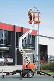 Workers in an orange lift basket, repairing a street light. Lift arm raised near a building.