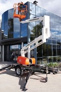 A person in an orange lift basket cleaning a glass building exterior with a white boom lift.