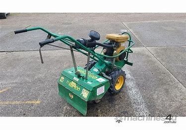 Green and yellow walk-behind garden tiller on concrete, with two handles and a rear engine.