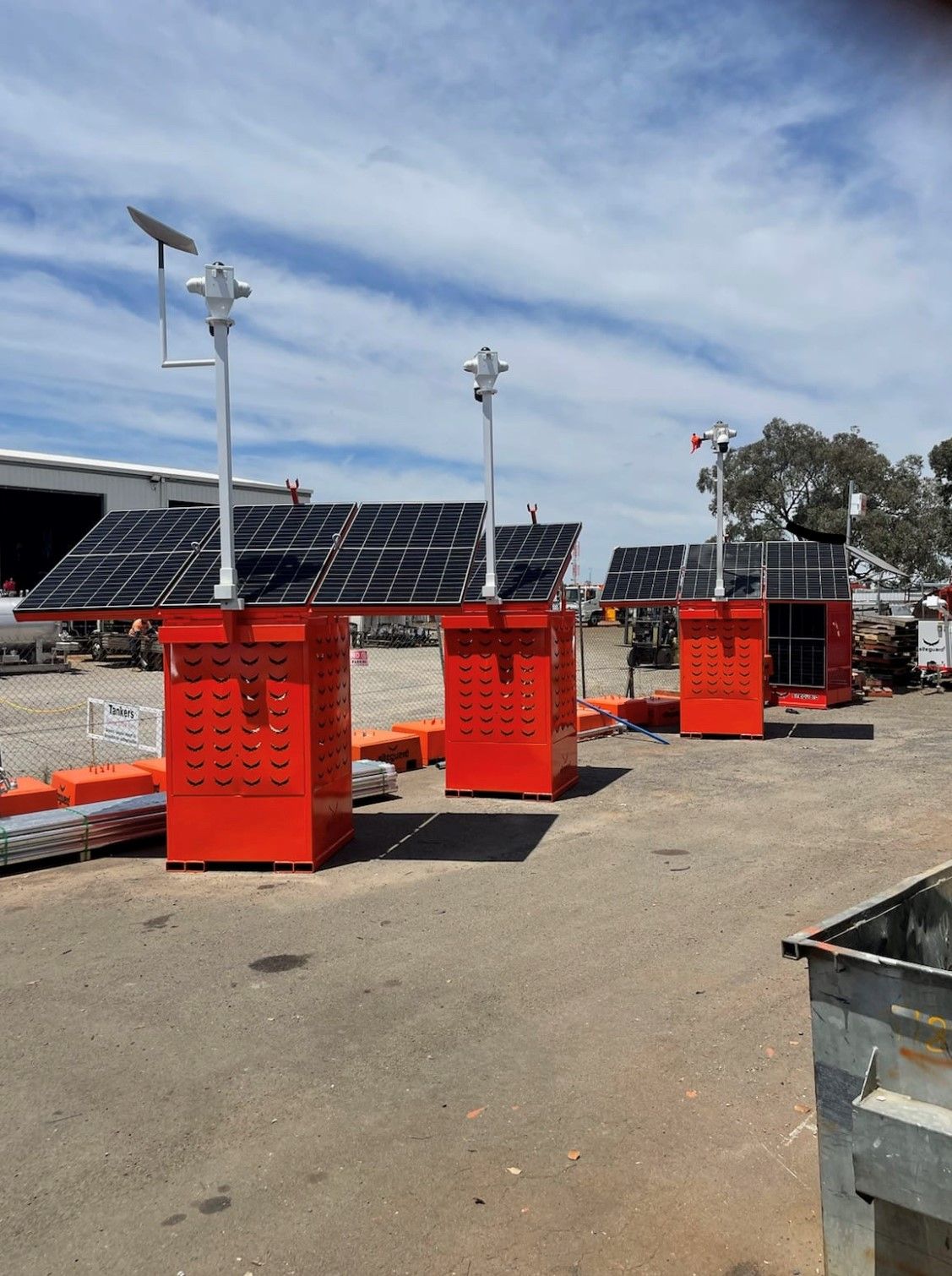 Three orange solar-powered monitoring stations with solar panels and cameras in a paved outdoor setting.