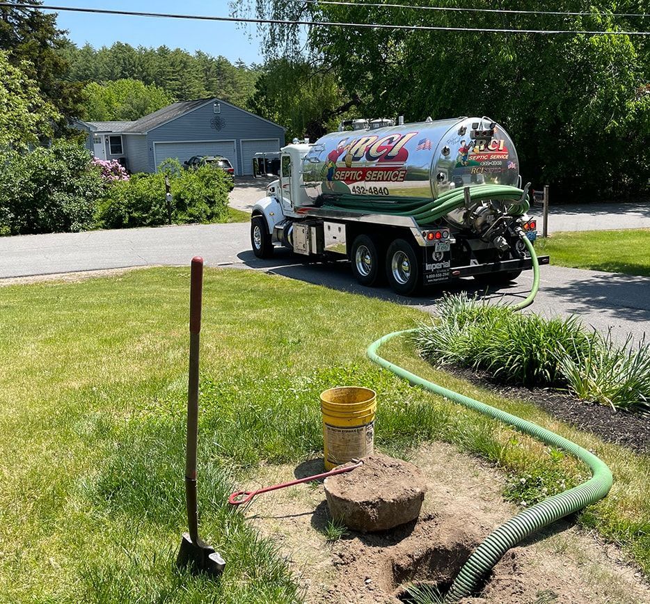 A septic tank truck pumping out a residential septic system in a suburban yard on a sunny day.