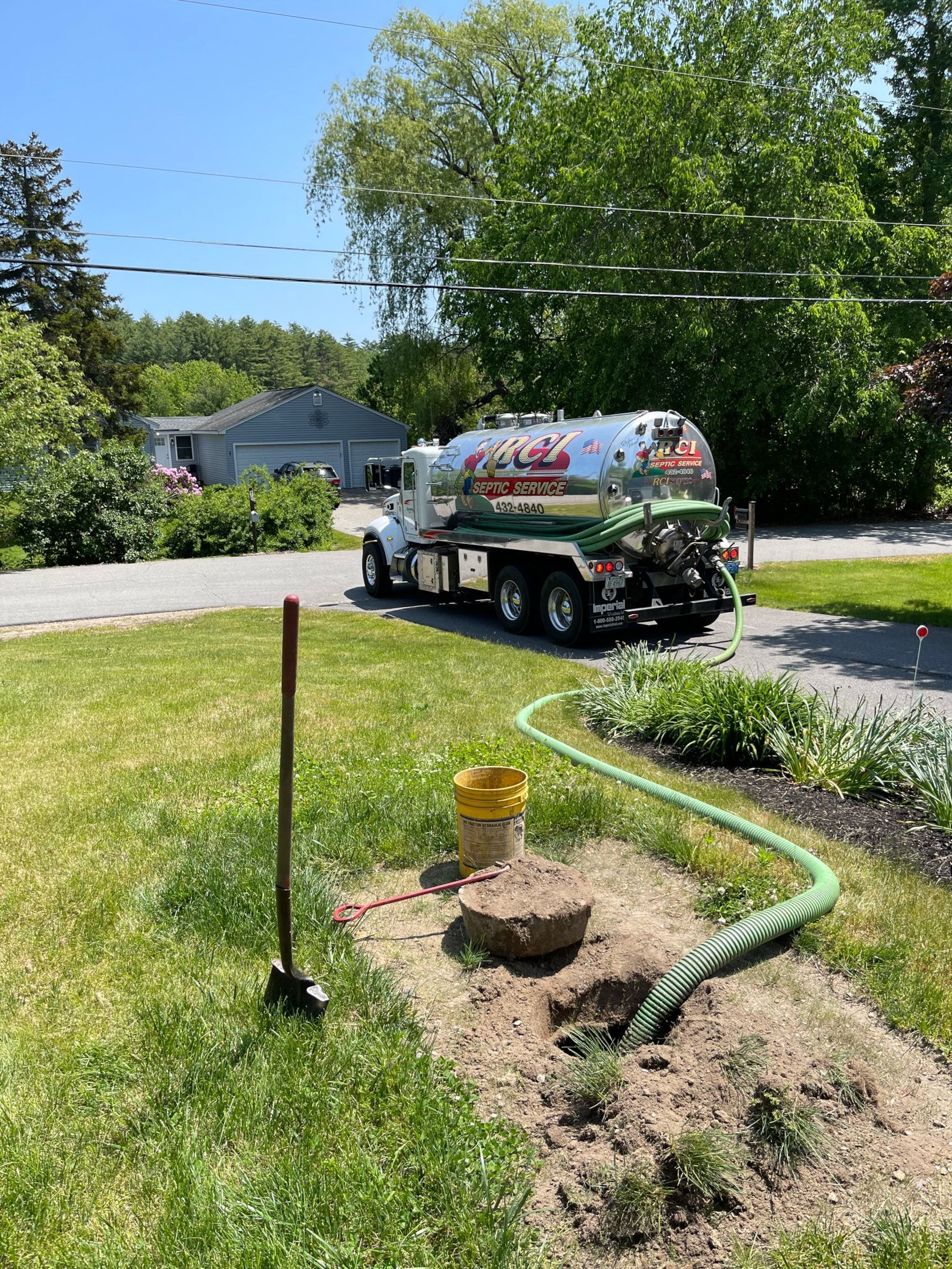 A septic tank truck is pumping water into a hole in a yard.