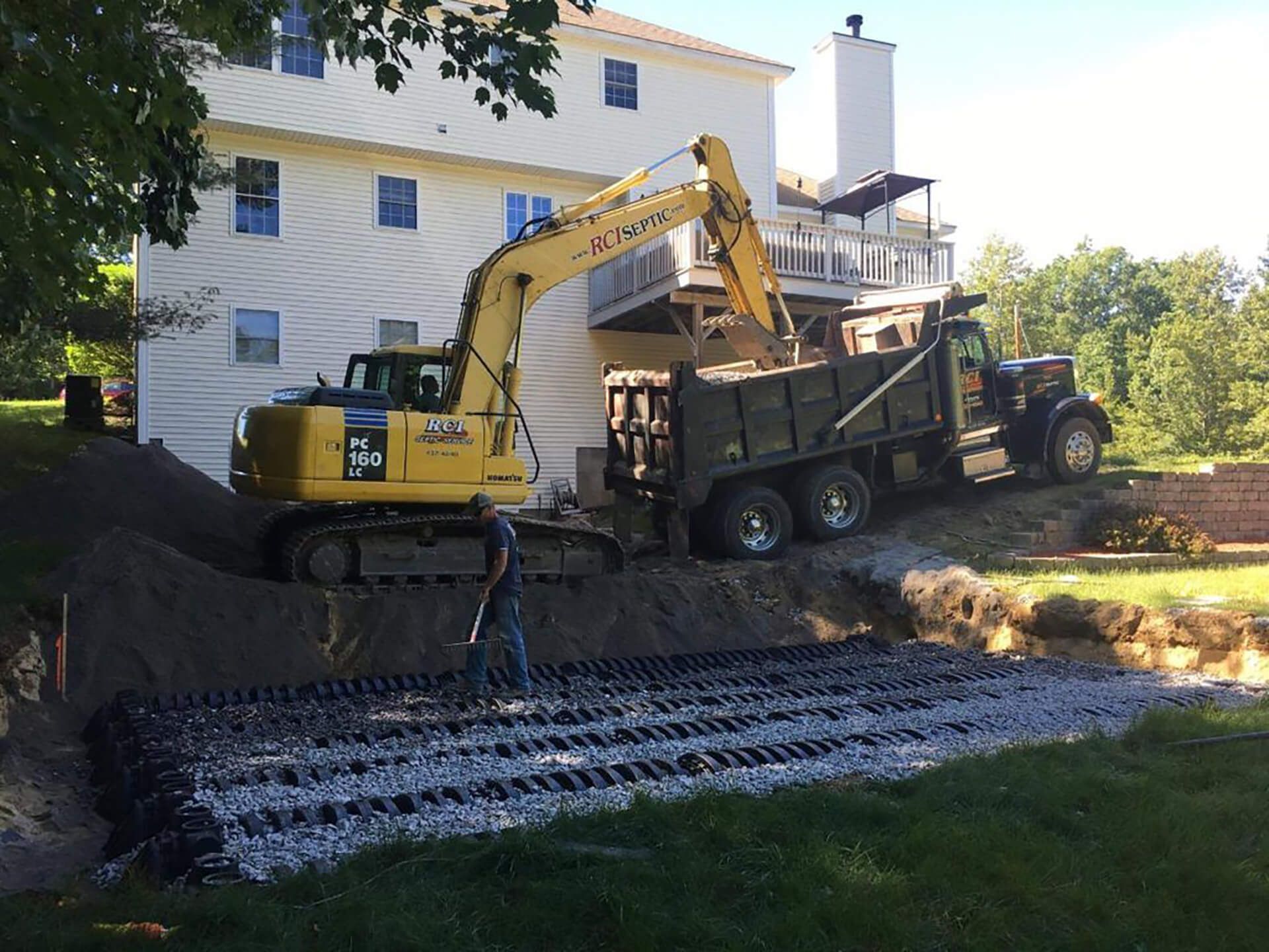 Excavator installing a new leach field during a septic system replacement at a New Hampshire home