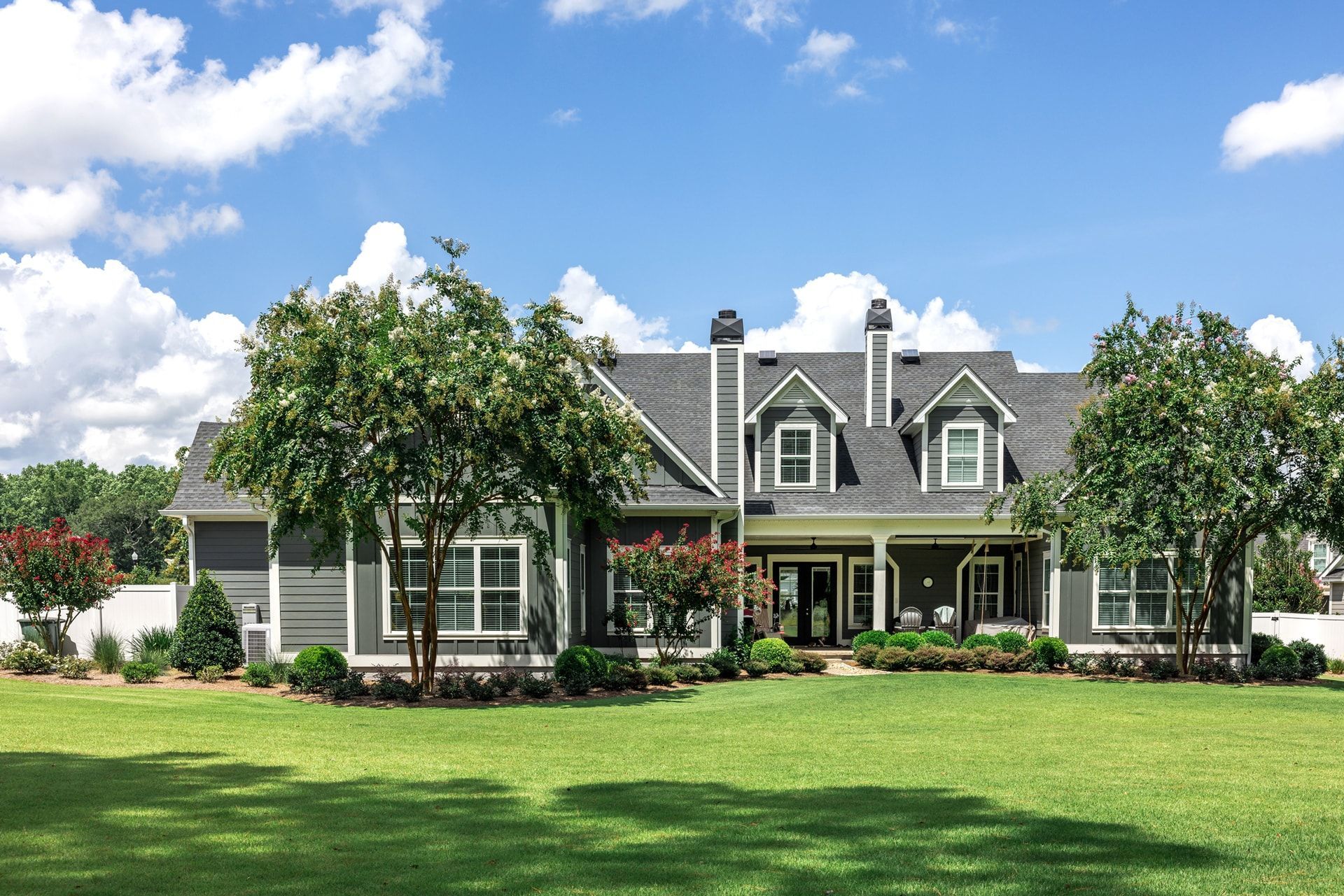 A large, gray house with a green lawn, blue sky, and some trees in front.