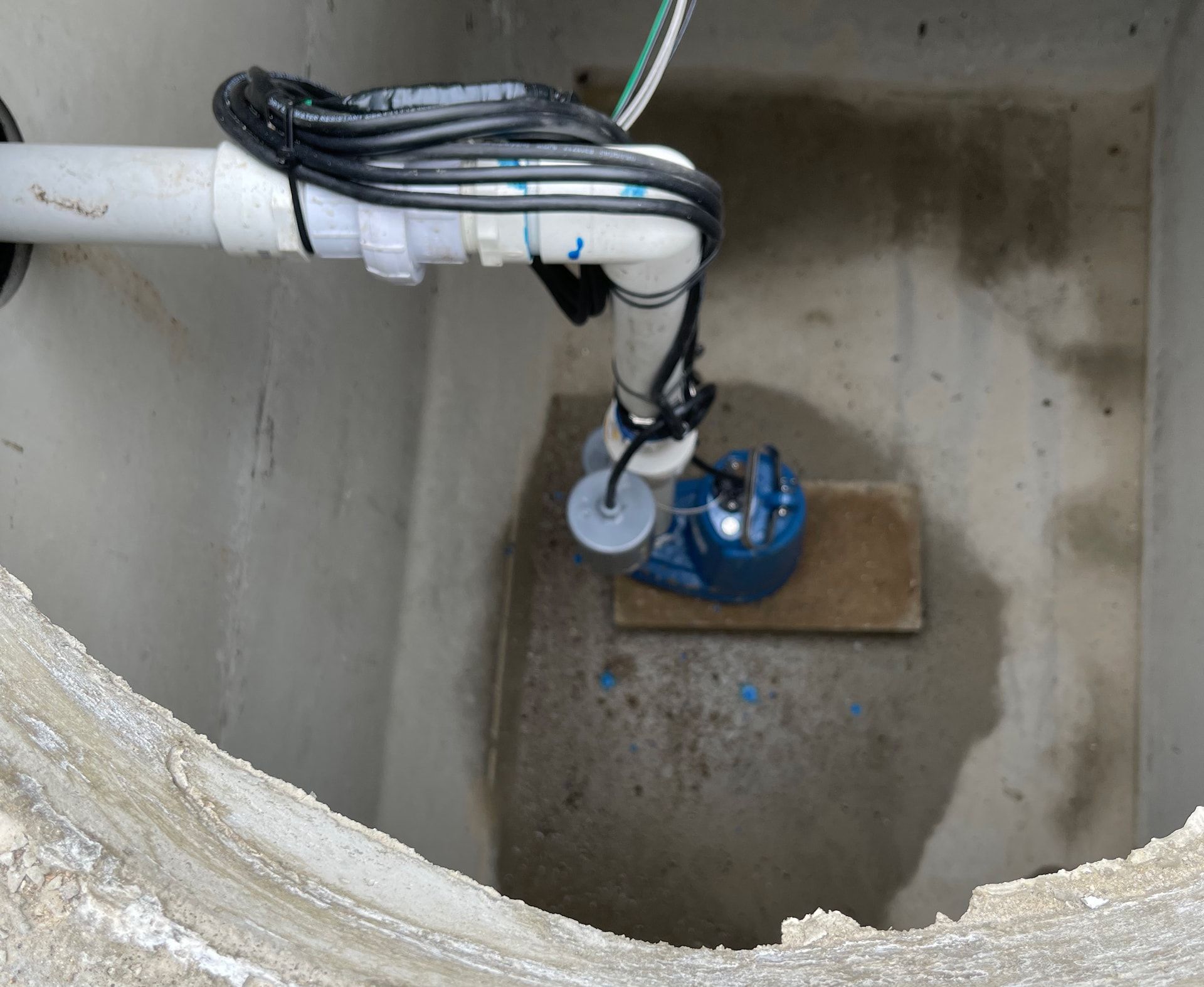Sump pump in a concrete pit, with white PVC pipe and electrical cables.