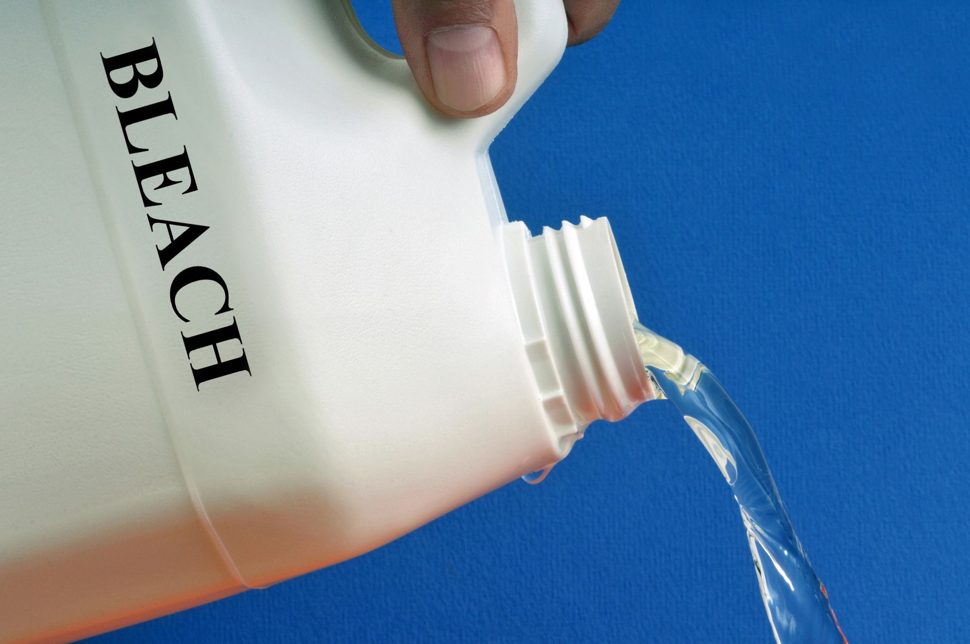 Hand pouring bleach from a white bottle with black label onto a blue background