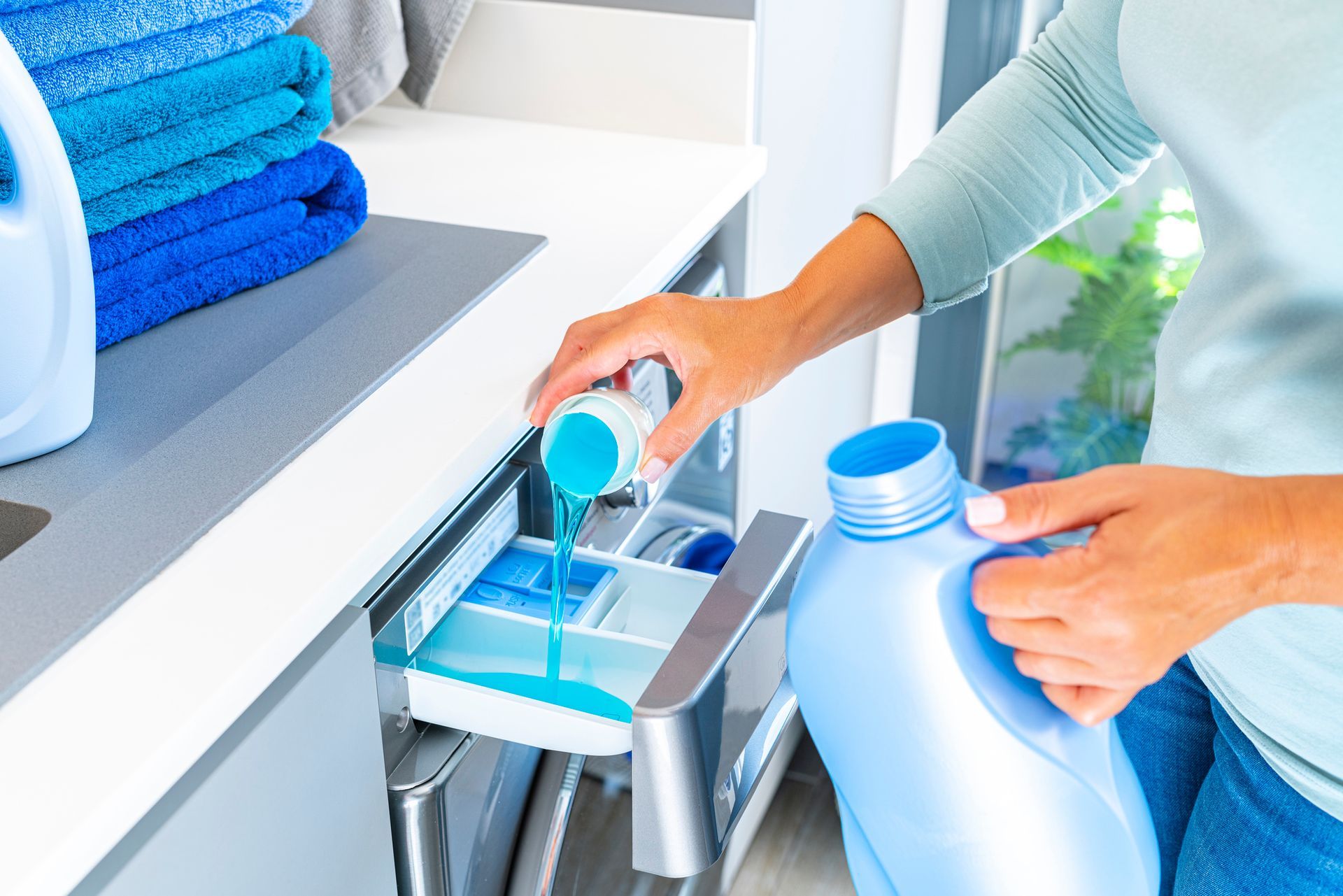Person pouring blue detergent into a laundry machine drawer from a white bottle
