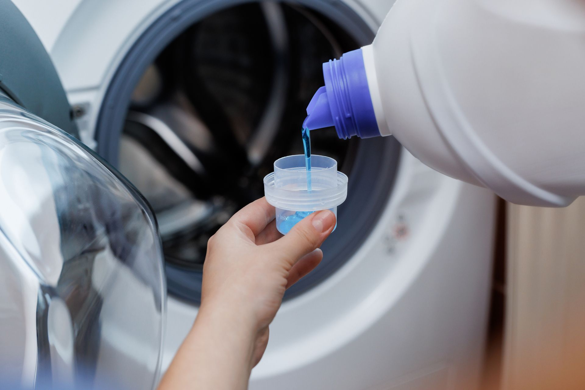 Laundry detergent being poured into a measuring cap near a washing machine
