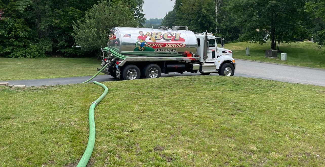 A septic tank truck is driving down a road with a green hose attached to it.
