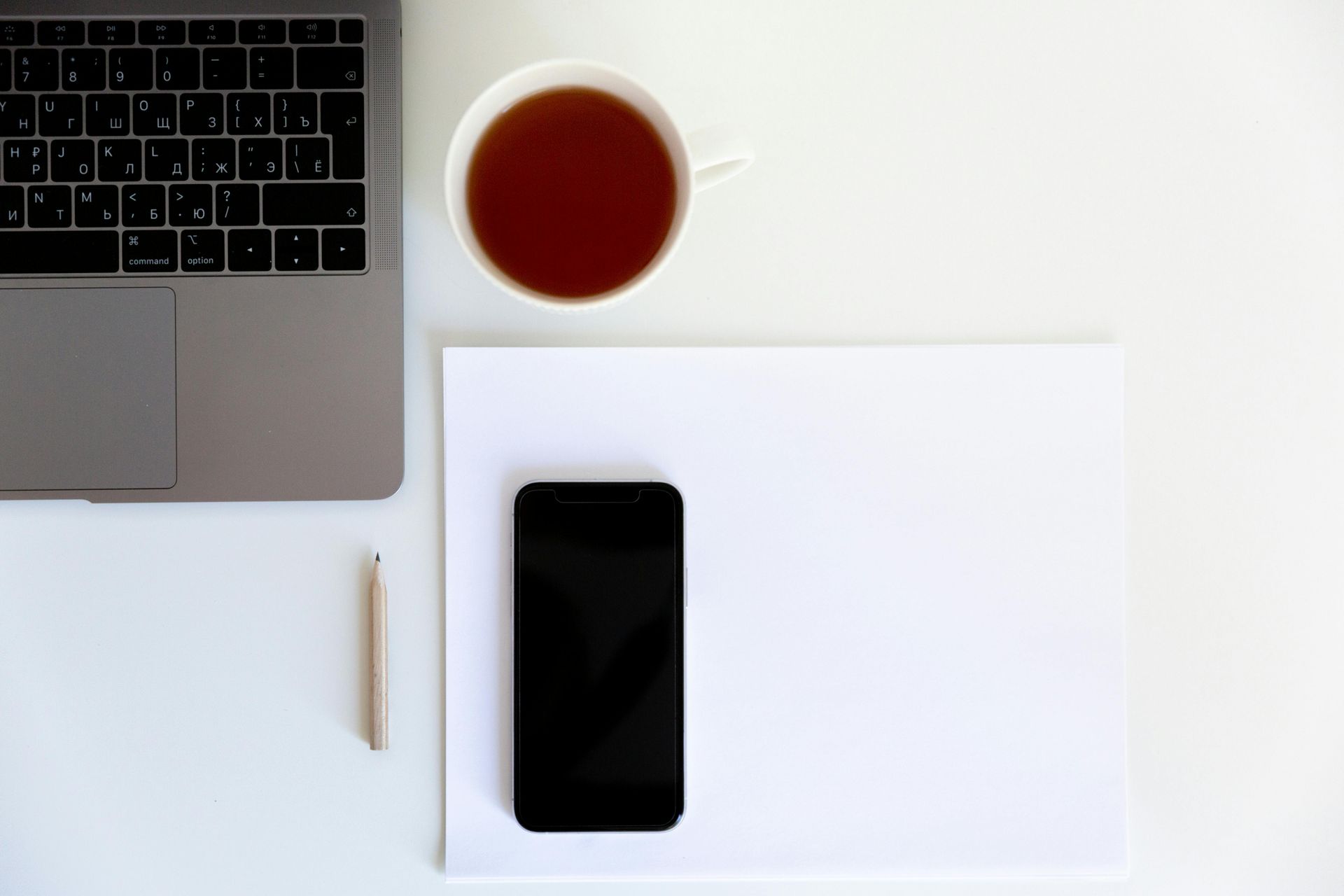 Computer portatile, tazza di tè, smartphone, penna e carta bianca su una superficie bianca.