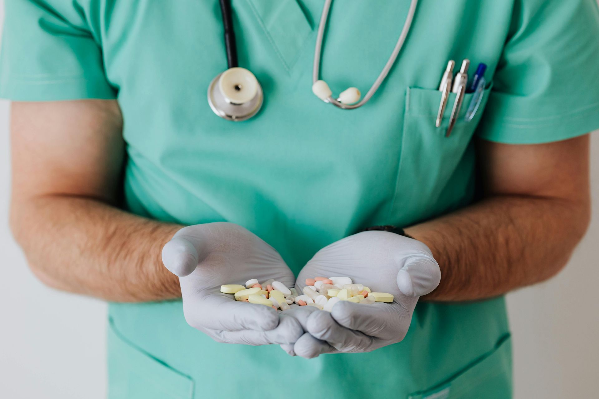 Medico in camice e guanti che tiene in mano delle pillole. Stetoscopio al collo.