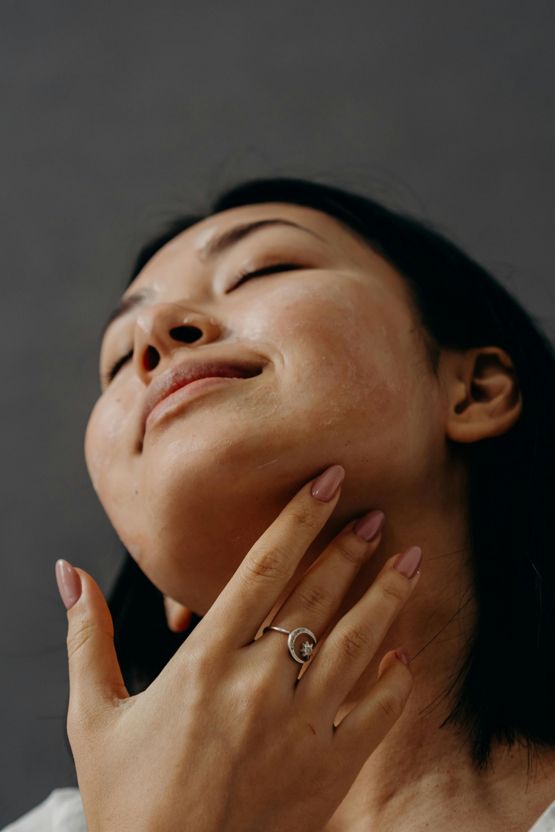 La persona si tocca il collo, con gli occhi chiusi, sorridendo e con un anello al dito.