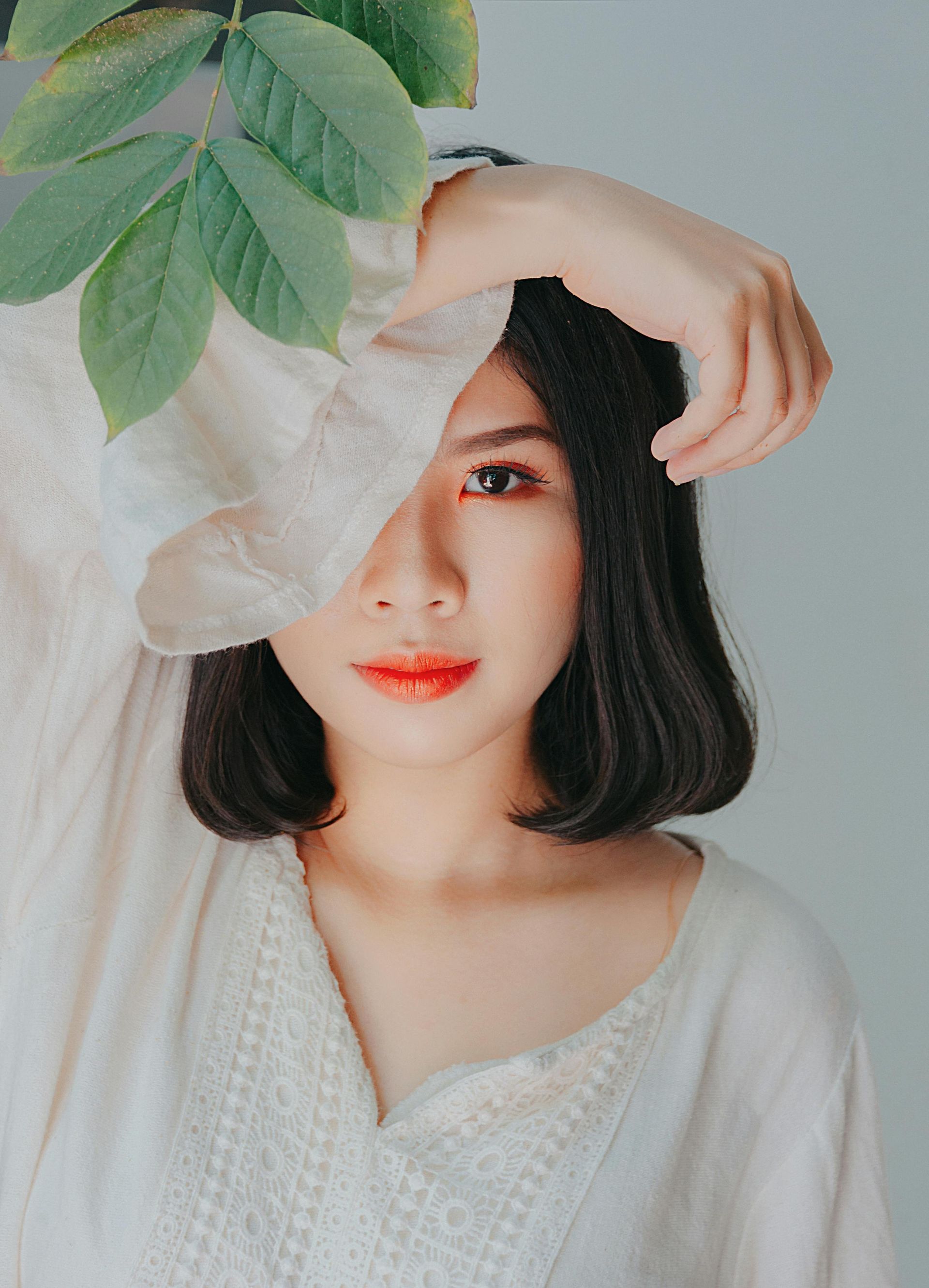 Donna con capelli neri, rossetto rosso acceso, che copre parzialmente il viso con un braccio, mentre lascia la casa sopra la testa.