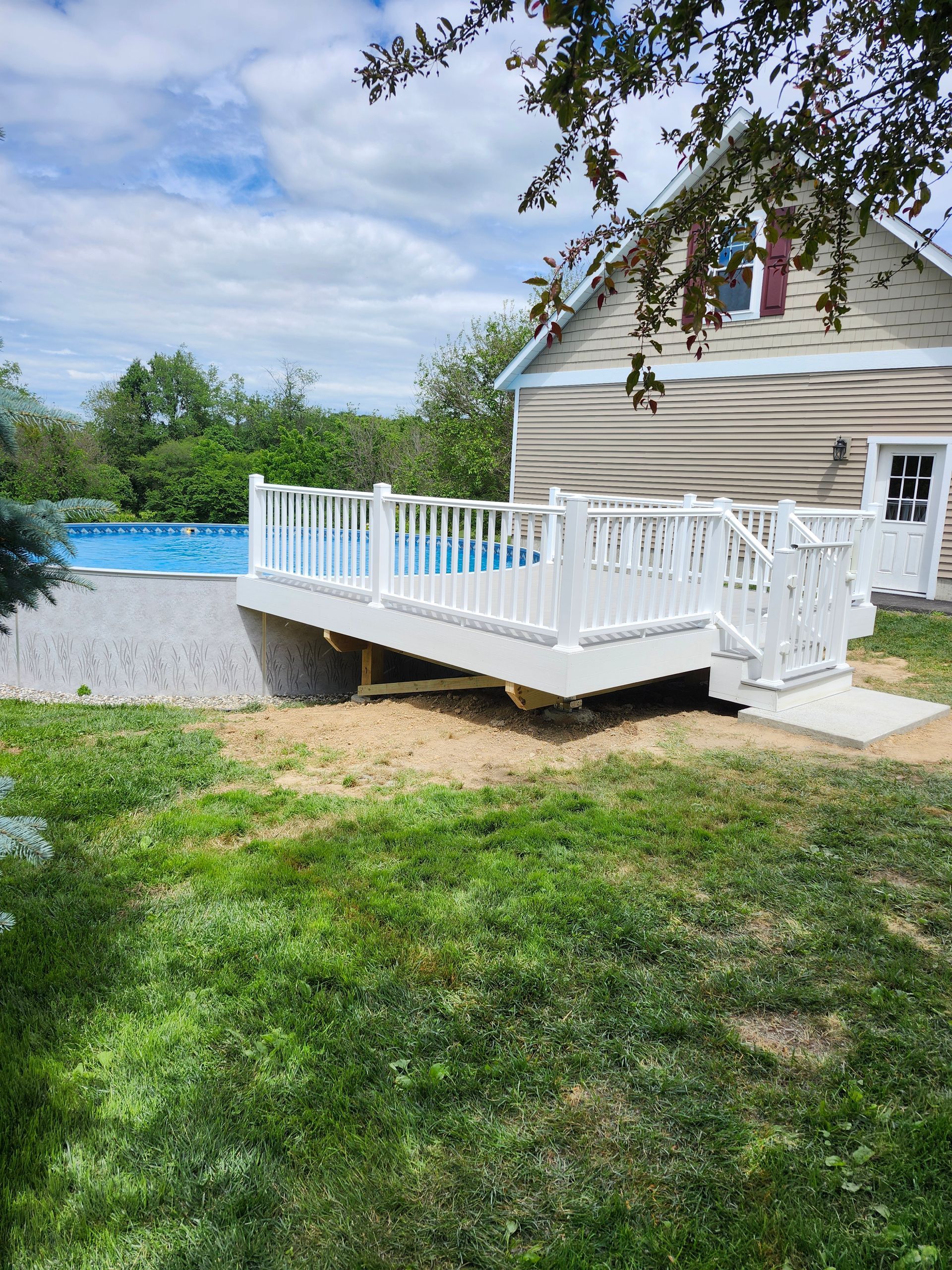 A white deck is sitting next to a house next to a pool.