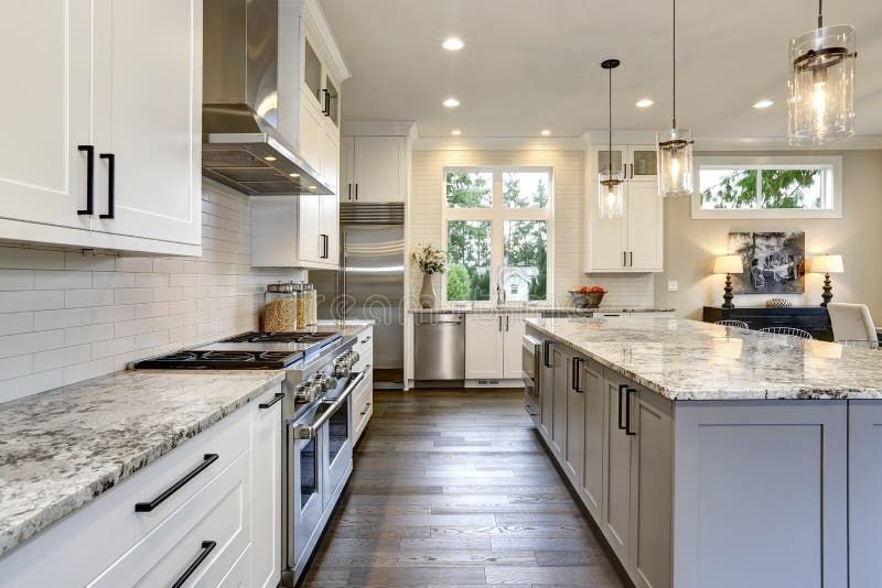 A kitchen with white cabinets, granite counter tops, stainless steel appliances and a large island.