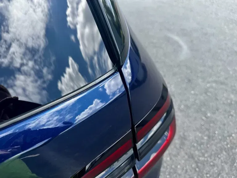 Close-up of a blue car’s rear quarter panel and taillight against a cloudy sky