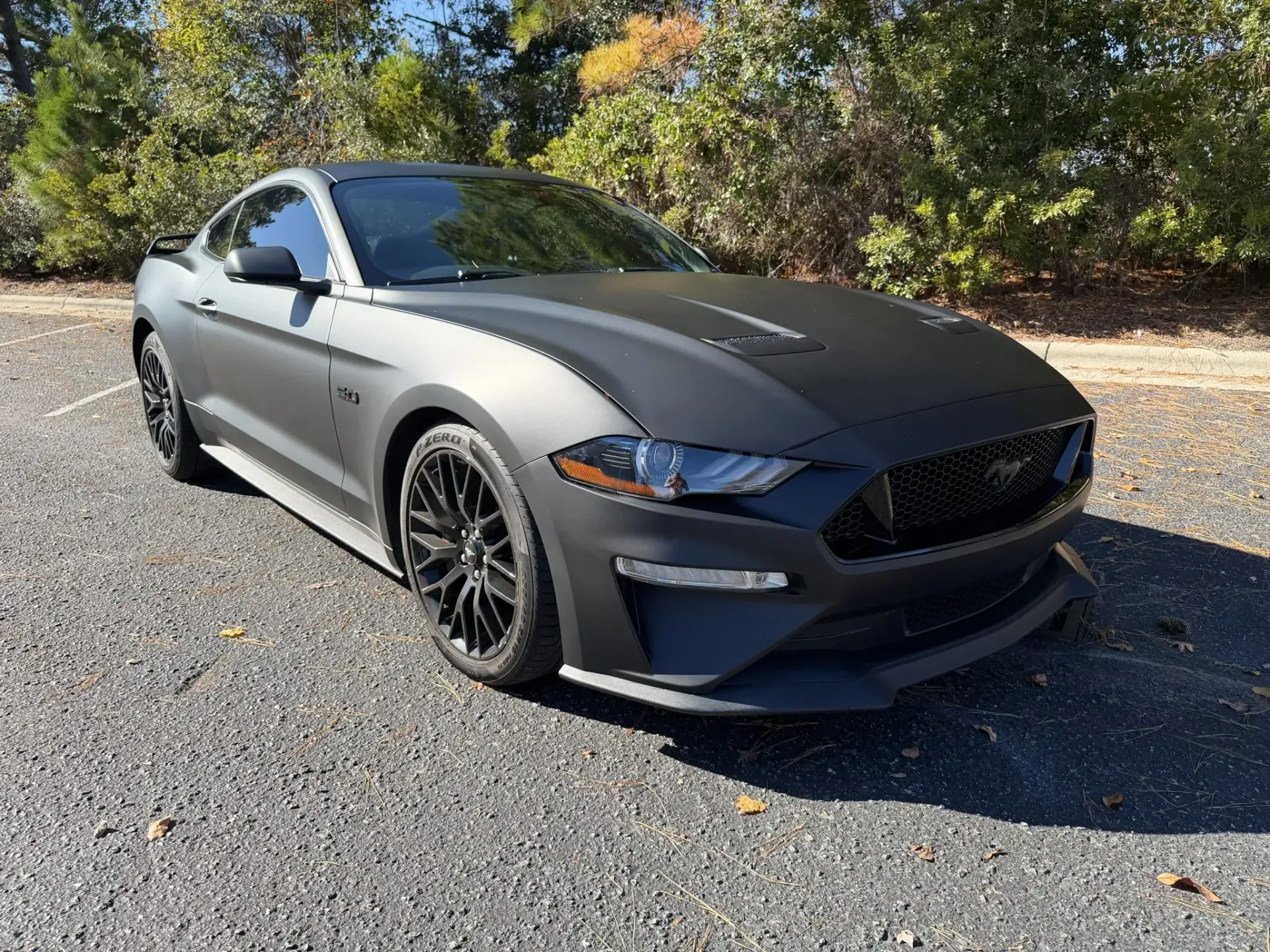 Matte gray sports coupe parked on gravel with trees in the background