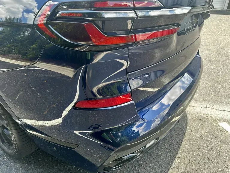 Close-up of the rear corner of a dark SUV with a cracked taillight and scuffed bumper after minor damage