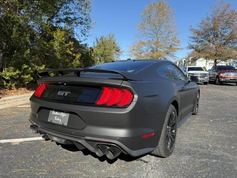 Gray Ford Mustang GT parked outdoors, rear three-quarter view in a sunny lot.