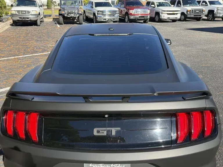 Rear view of a black Ford Mustang GT parked in a lot, with red taillights visible.