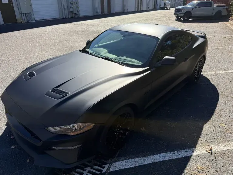 Black sports car parked on asphalt in bright sunlight, viewed from the front-left angle